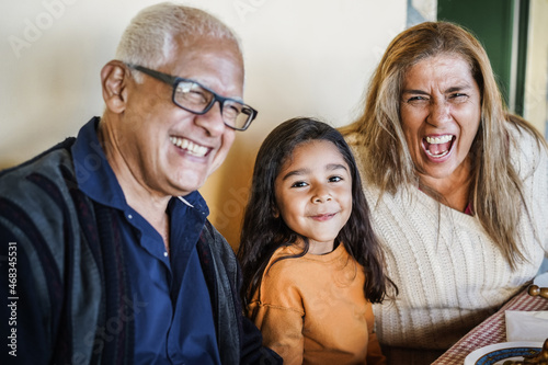 Happy latin girl having fun eating with her grandparents at home - Focus on little kid face