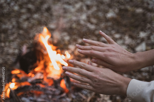 A woman warms her hands over a fire in a campsite. Journey to the forest