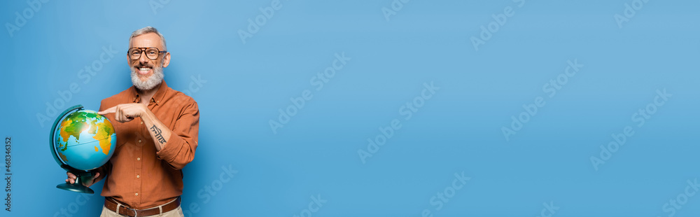 happy middle aged teacher in glasses pointing with finger at globe on blue, banner happy middle aged teacher in glasses pointing with finger at globe on blue, banner