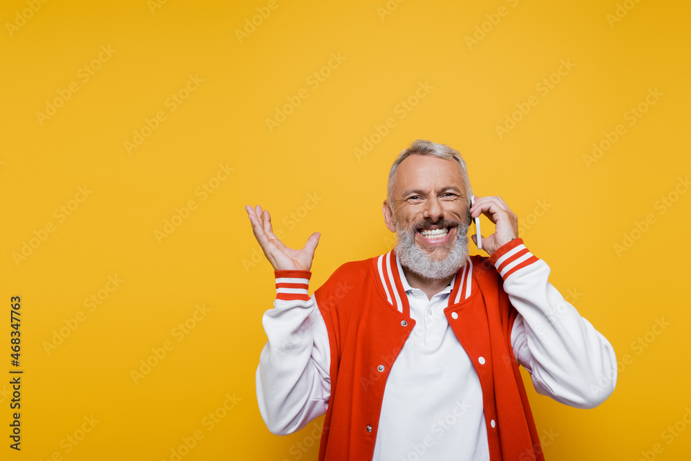 happy middle aged man talking on smartphone and gesturing isolated on yellow happy middle aged man talking on smartphone and gesturing isolated on yellow