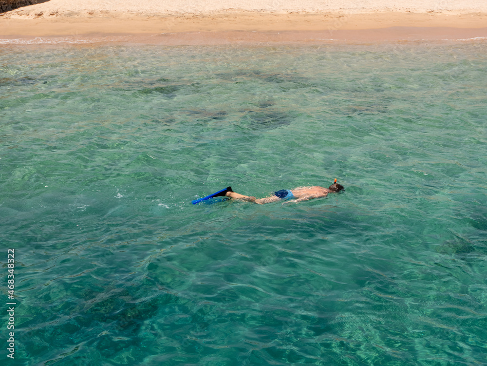 Man with a snorkel, mask and fins swims in the azure water of the Red Sea.