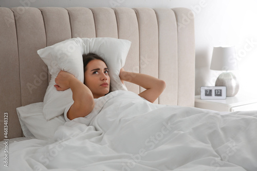 Unhappy young woman covering ears with pillow in bed at home. Noisy neighbours
