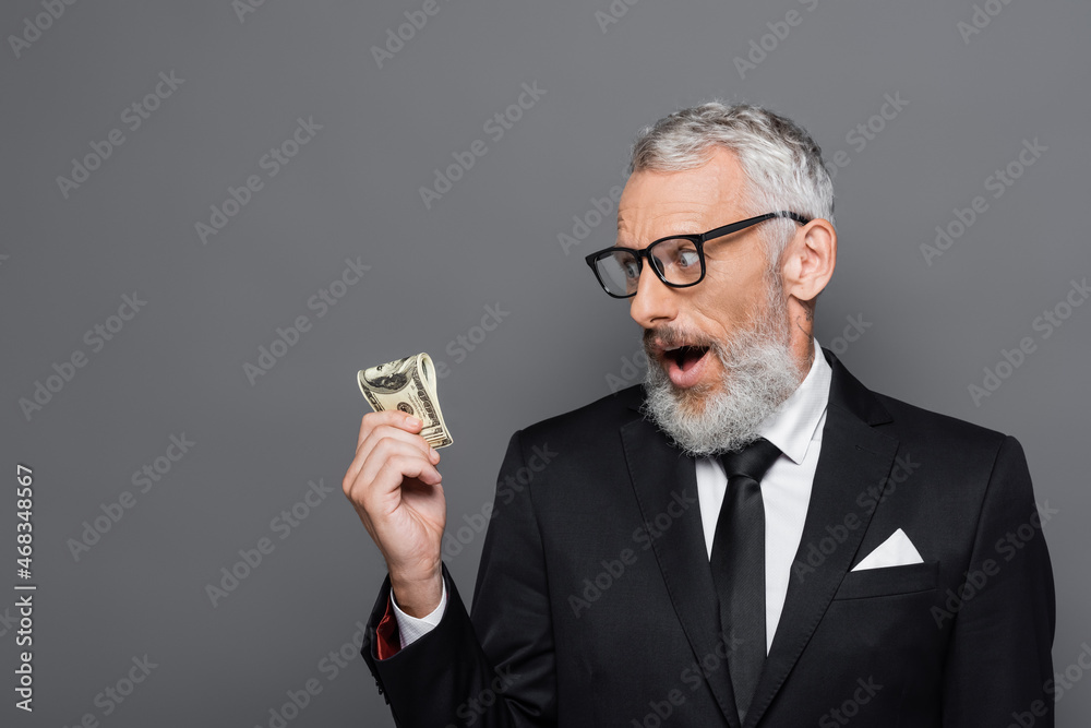 shocked middle aged businessman looking at dollar banknotes isolated on grey