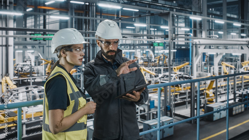 Male Specialist and Female Car Factory Engineer in High Visibility Vests Using Tablet Computer. Automotive Industrial Manufacturing Facility Working on Vehicle Production. Diversity on Assembly Plant.