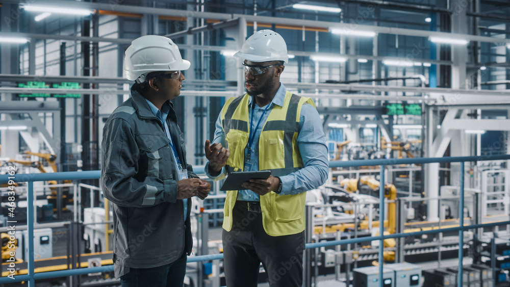 Multiethnic Manager and African American Car Factory Engineer in Uniform Using Tablet Computer. Automotive Industry 4.0 Manufacture Employees Discuss Work on Vehicle Assembly Plant. Multiethnic Manager and African American Car Factory Engineer in Uniform Using Tablet Computer. Automotive Industry 4.0 Manufacture Employees Discuss Work on Vehicle Assembly Plant.