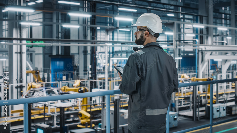 Car Factory Engineer in Work Uniform Using Tablet Computer. Automotive Industrial Manufacturing Facility Working on Vehicle Production with Robotic Arms Technology. Automated Assembly Plant.