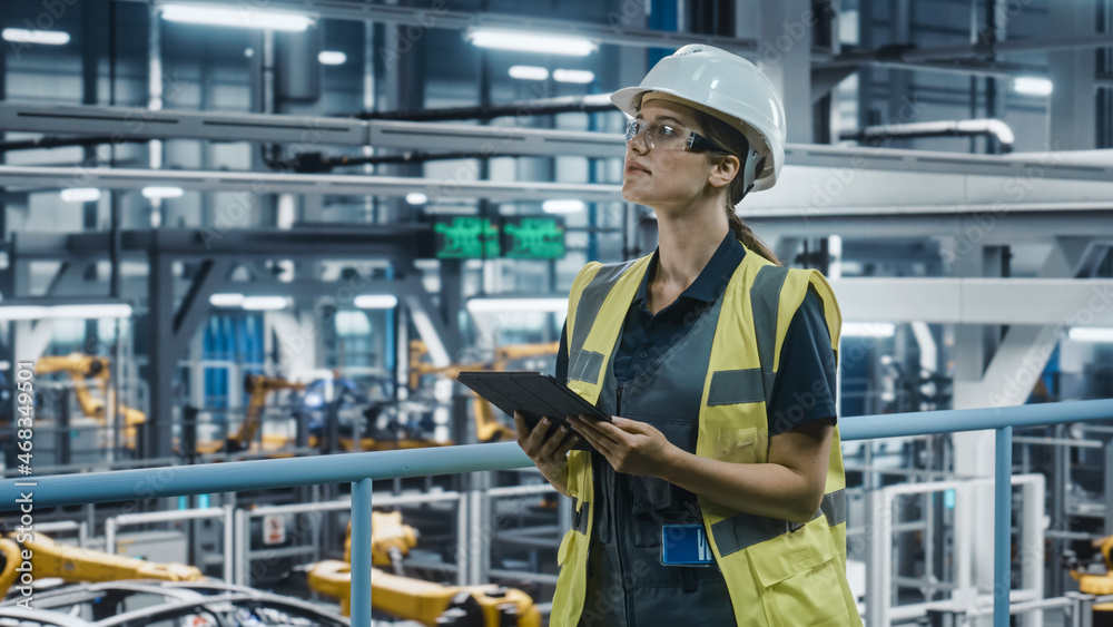 Female Car Factory Engineer in High Visibility Vest Using Tablet Computer. Automotive Industrial Manufacturing Facility Working on Vehicle Production with Robotic Technology. Automated Assembly Plant. Female Car Factory Engineer in High Visibility Vest Using Tablet Computer. Automotive Industrial Manufacturing Facility Working on Vehicle Production with Robotic Technology. Automated Assembly Plant.