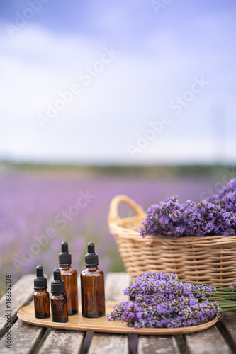 Essential lavender oil in the bottle with dropper on the gray wooden desk. Vertical close-up.
