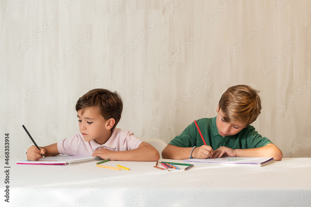 Two children doing homework at school, drawing with crayons Two children doing homework at school, drawing with crayons