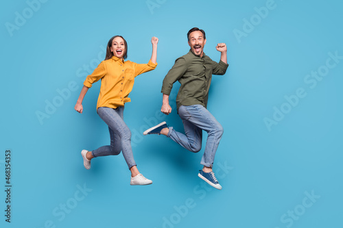 Full size profile photo of two delighted persons raise fists celebrate success triumph isolated on blue color background