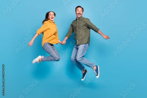 Full size photo of mature cheerful man and woman jump up husband wife enjoy isolated on blue color background
