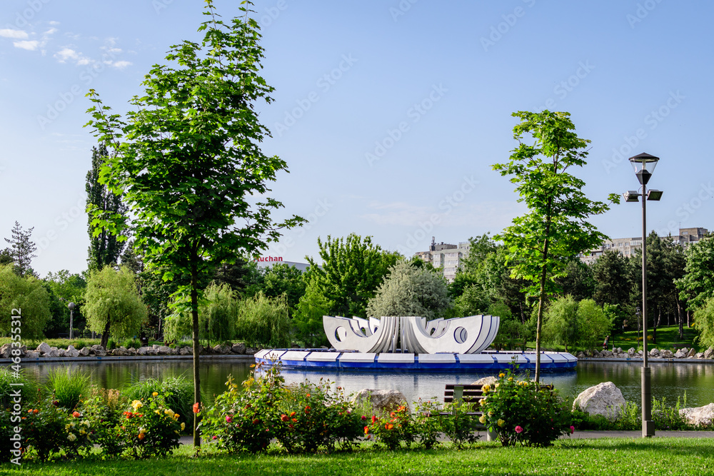 Landscape with the lake, decorative fountain and vivid green trees in Drumul Taberei Park (Parcul Drumul Taberei) also known as Moghioros Park, in Bucharest, Romania, in a sunny spring day.