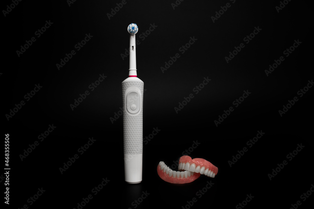 Dental care with an electric brush. Dentures and an electric brush on a black background