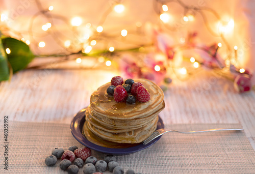 Delicious American pancakes with syrup and berries  blueberries  raspberries on a pink background with flowers with blur bokeh 
