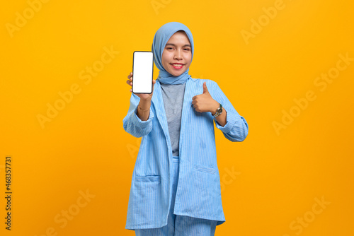 Smiling young Asian woman showing smartphone blank screen and makes thumbs up sign