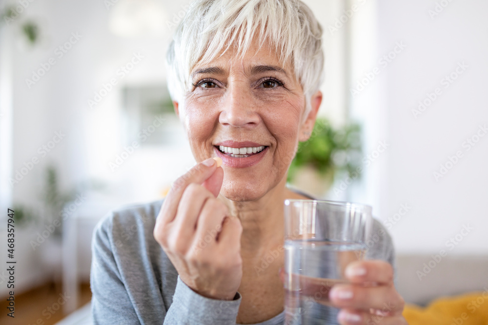 Smiling happy healthy middle aged 50s woman holding glass of water taking dietary supplement vitamin pill. Old women multivitamins antioxidants for anti age beauty. Smiling happy healthy middle aged 50s woman holding glass of water taking dietary supplement vitamin pill. Old women multivitamins antioxidants for anti age beauty.