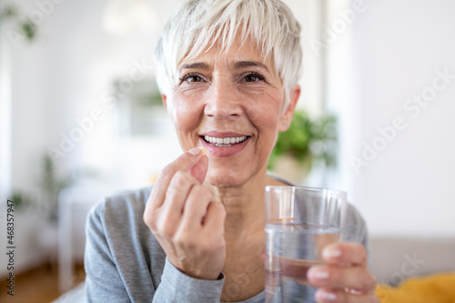 Fotografía Smiling happy healthy middle aged 50s woman holding glass of water taking dietary supplement vitamin pill