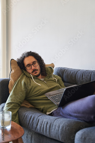 Canvas Print Vertical medium shot of young man sleeping on the sofa while working with laptop