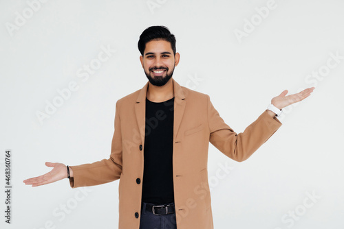 Young indian man standing over isolated white background smiling showing both hands open palms, presenting and advertising comparison and balance