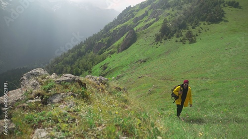 A male tourist climbs the mountain in a yellow raincoat, with a large backpack on his back. Tourism.