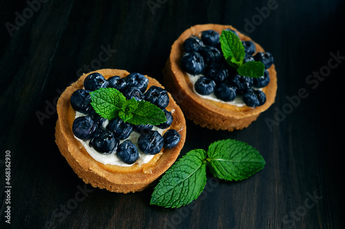 Tarts with blueberries and mint on dark wood background