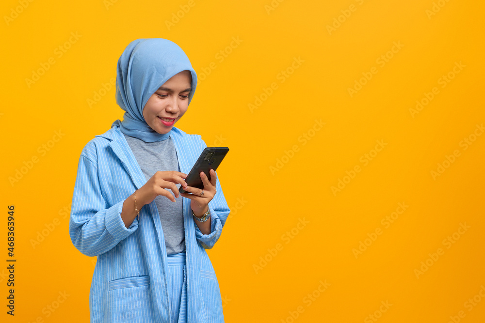 Cheerful young Asian woman looking at mobile phone isolated over yellow background Cheerful young Asian woman looking at mobile phone isolated over yellow background