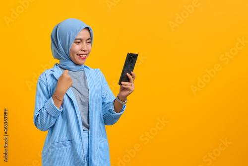 Cheerful young Asian woman looking at mobile phone isolated over yellow background © Sewupari Studio