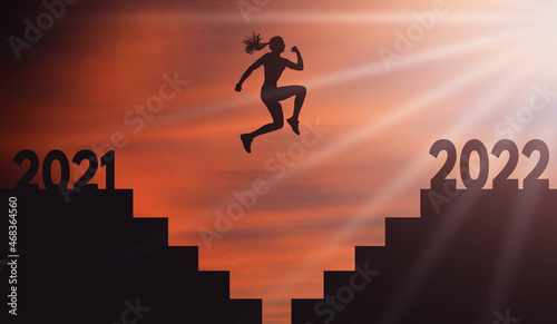 Young Woman Jumping From 2021 To 2022 Over Stair Gap with a Big Jump at Orange Sunset. Female silhouette Jump on Stairs From Dark side to light Side. 2021 end 2022 New start. Hope and Girl Success 