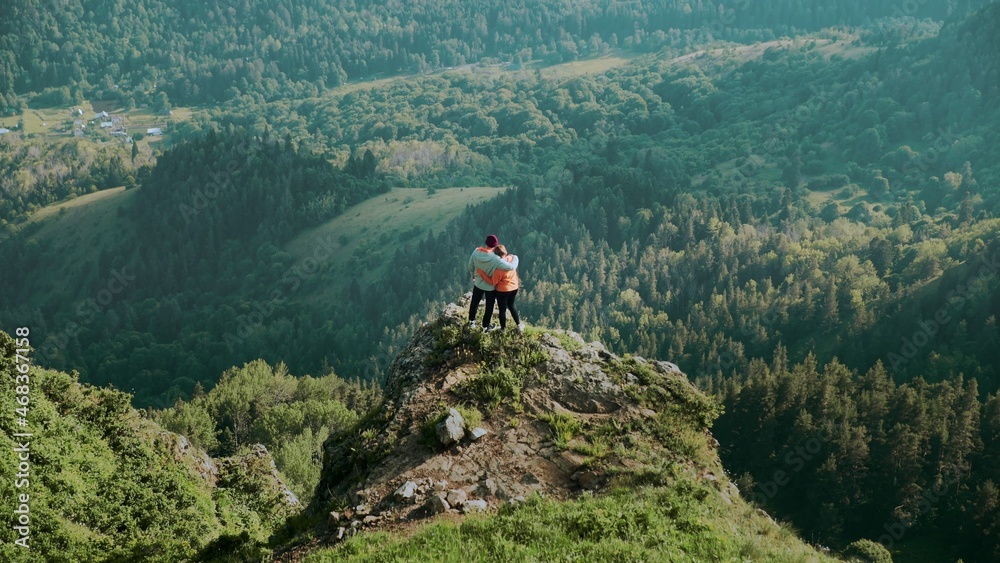 A young woman approaches a man to a cliff in a mountainous area. Travel