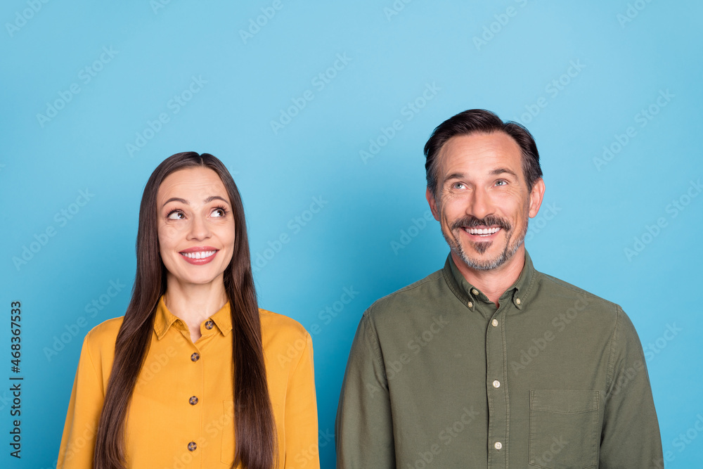 Photo of cheerful curious married man and woman look empty space up isolated on blue color background Photo of cheerful curious married man and woman look empty space up isolated on blue color background