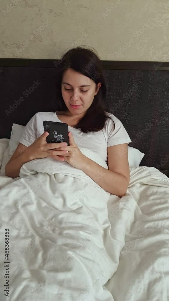 woman laying in bed surfing internet on the phone woman laying in bed surfing internet on the phone