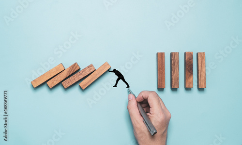 Businessman hand writing black man pushing rectangle block which falling to stop dominos others rectangle standing on blue background. Risk and crisis management concept.