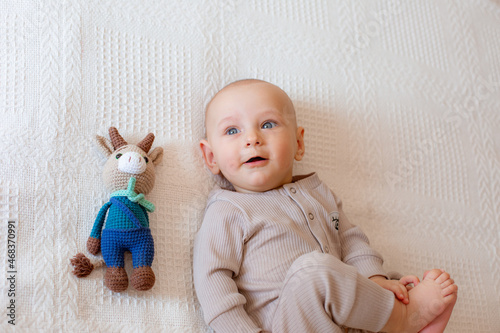 baby boy with blue eyes lies next to a toy at home in the bedroom on the bed, top view
