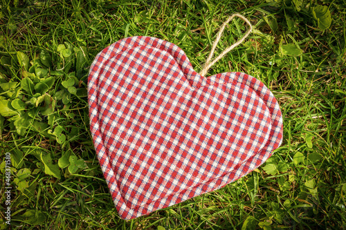 Close-up of a red  white and blue heart  made of cloth above the green grass of a meadow.