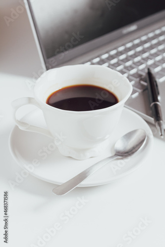 Cup of coffee and laptop on white table.