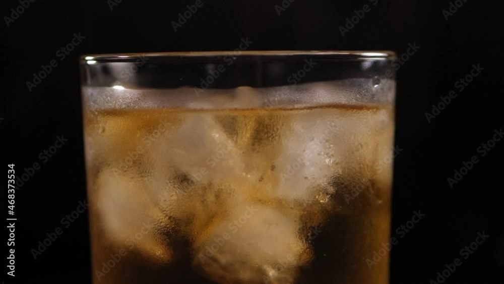 Close-up of a full glass of whiskey with ice slowly rotates on a black background. Slow motion. Image of a chilled alcoholic drink with ice. Close-up of a full glass of whiskey with ice slowly rotates on a black background. Slow motion. Image of a chilled alcoholic drink with ice.
