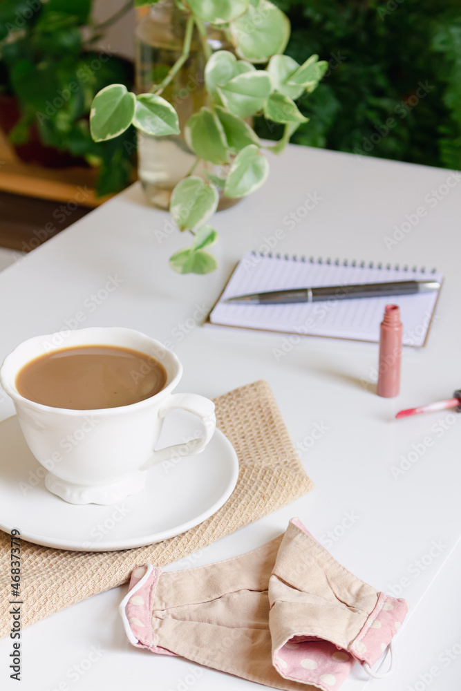 Breakfast with coffee, notepad, lipstick and mask on white table. Cafe, restaurant on pandemic concept. Breakfast with coffee, notepad, lipstick and mask on white table. Cafe, restaurant on pandemic concept.
