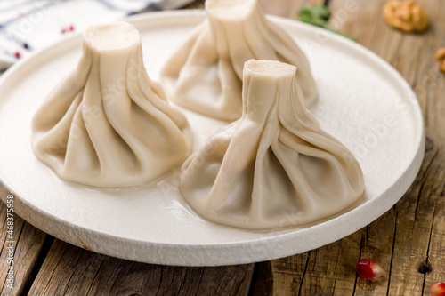 Khinkali with lamb on white plate, georgian cuisine on wooden table © Алиса Королевская