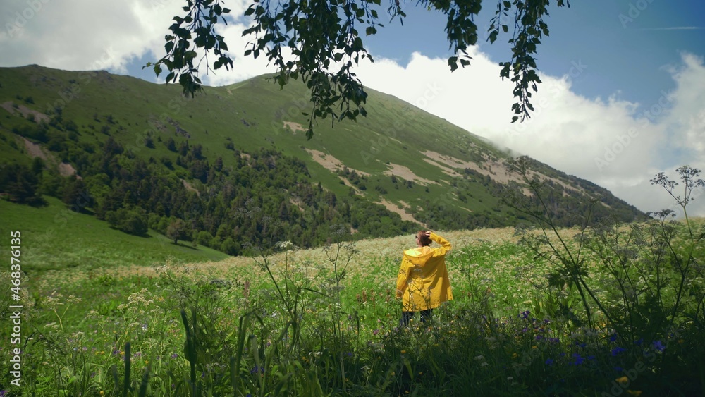 A young man in a yellow raincoat is happily picking flowers in a meadow and enjoying the scenery in mountainous areas. Travel and tourism A young man in a yellow raincoat is happily picking flowers in a meadow and enjoying the scenery in mountainous areas. Travel and tourism