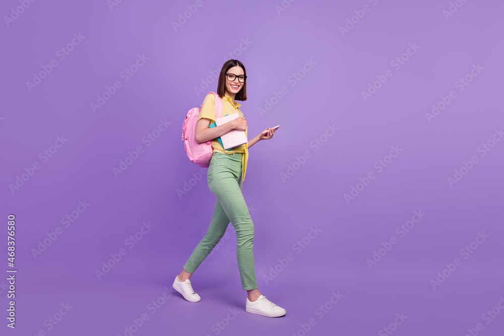 Full size profile side photo of young girl go university use smartphone courses academic isolated over purple color background Full size profile side photo of young girl go university use smartphone courses academic isolated over purple color background