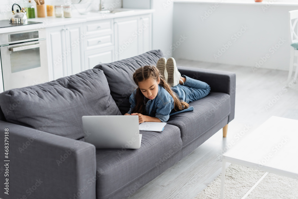 Child looking at notebook near laptop during online education at home