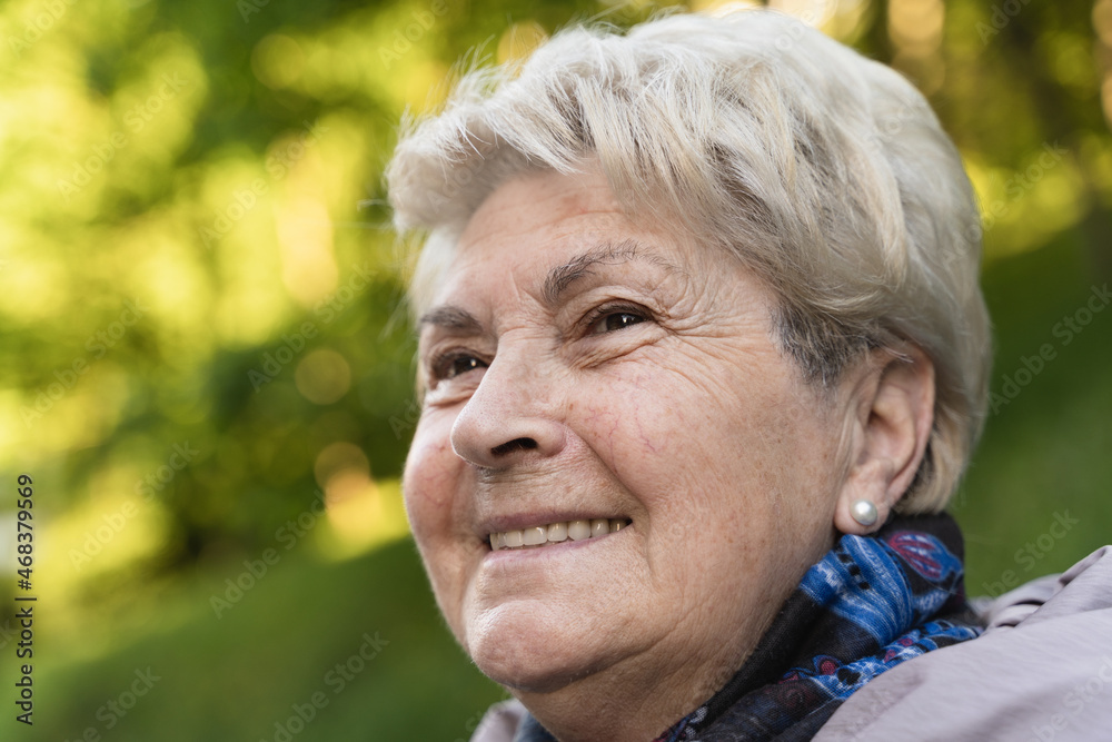 Portrait of senior woman with a vision look in her eyes at park during fall season. Blonde young looking lady with positive thinking look. Autumn fashion sales concept