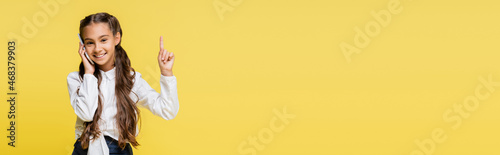 Foto Smiling schoolkid in shirt talking on smartphone and pointing with finger isolat