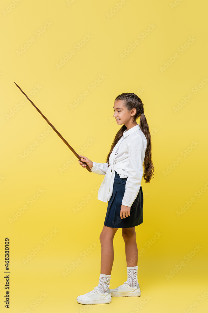 Full length of schoolchild in skirt holding pointer on yellow background Full length of schoolchild in skirt holding pointer on yellow background