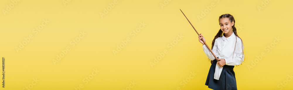Smiling schoolkid holding pointer isolated on yellow, banner