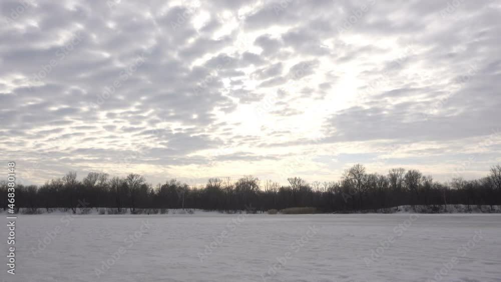 Gray clouds in time laps in the winter sky over the snow-covered river and forest. 