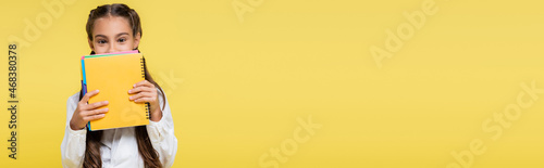 Fotografía Schoolkid covering face with notebooks isolated on yellow, banner