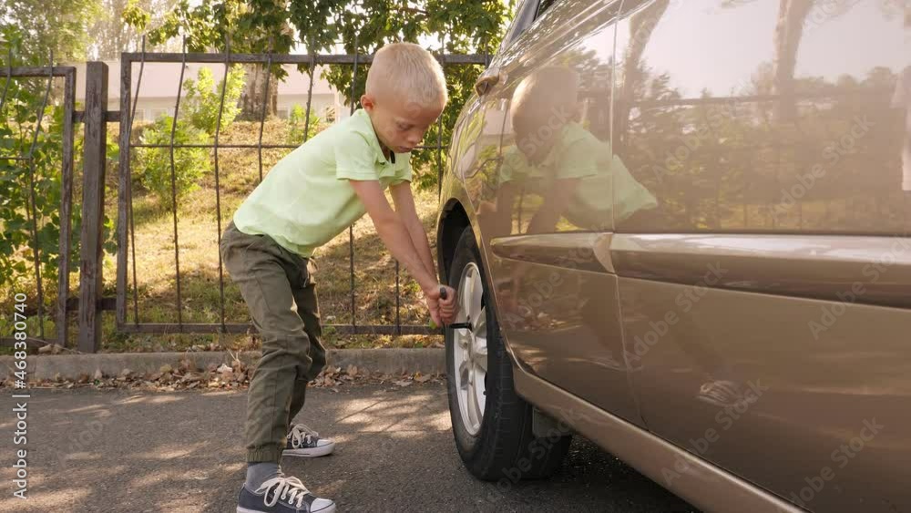 A little boy of eight years old is fixing a wheel on a car, he is trying to unscrew the bolts on the wheel to replace the tires. A little boy of eight years old is fixing a wheel on a car, he is trying to unscrew the bolts on the wheel to replace the tires.