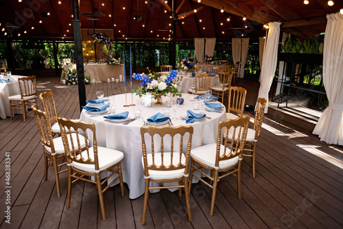 Festive wedding, table setting with blue linen napkins, candles, golden chairs, and fresh bouquets of flowers. Wedding decorations. Restaurant menu concept. Soft selective focus.