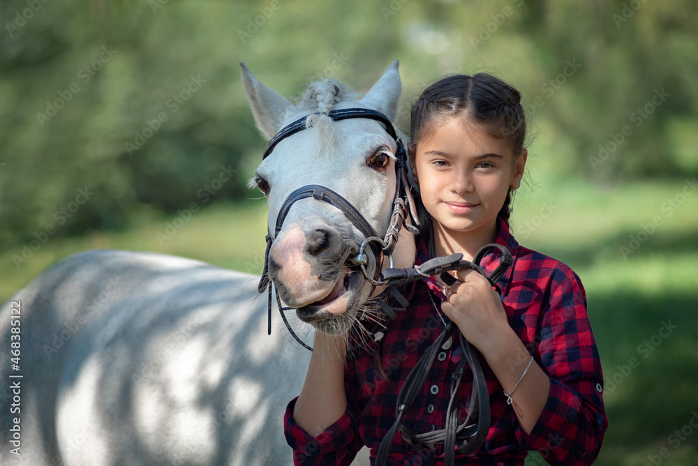 Obraz premium portrait of a beautiful teenage girl with a white horse in nature while walking in the park or in the woods. close-up